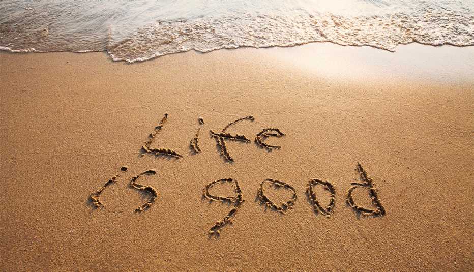 Palabras en inglés sobre la arena de una playa que dice la vida es buena.