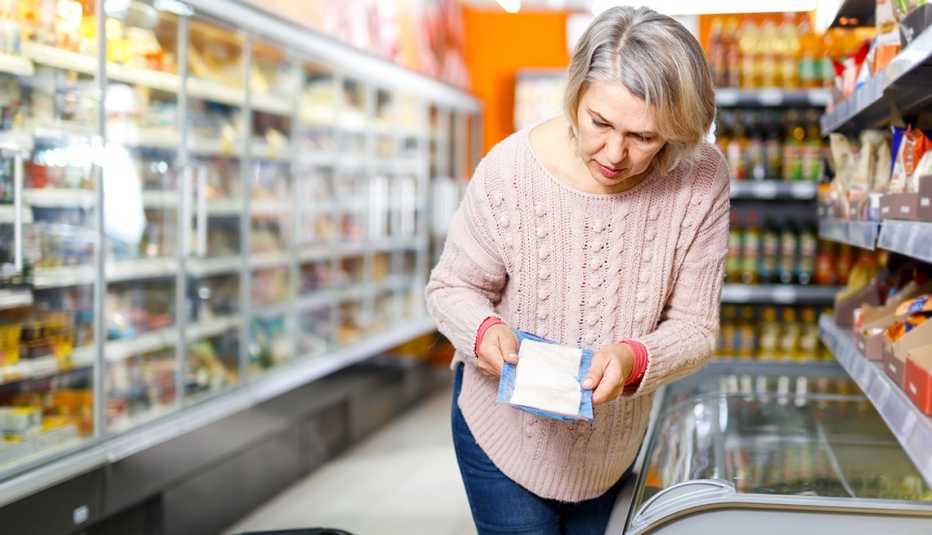 Mujer mayor sostiene un producto con sus manos en un supermercado.