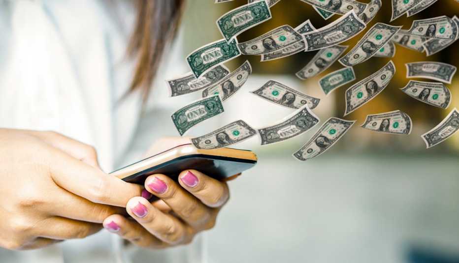 Manos de una mujer sosteniendo un teléfono móvil con dólares volando.
