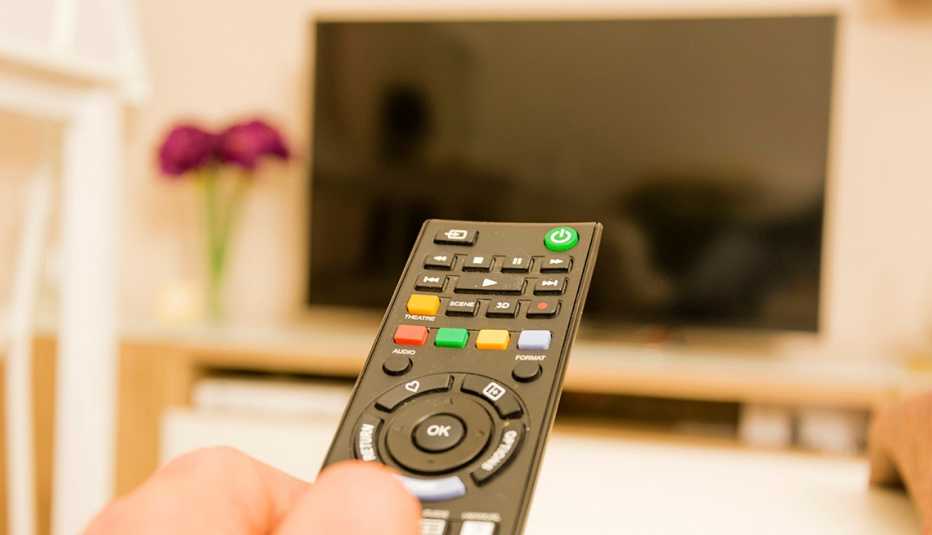 Un control remoto de televisión sostenido en una habitación iluminada mientras se apunta a un televisor.