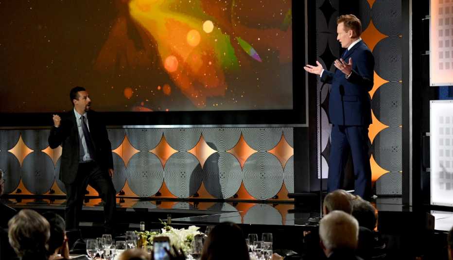 Conan O Brien abre sus manos cuando Adam Sandler llega al escenario de Movies for Grownups Awards.