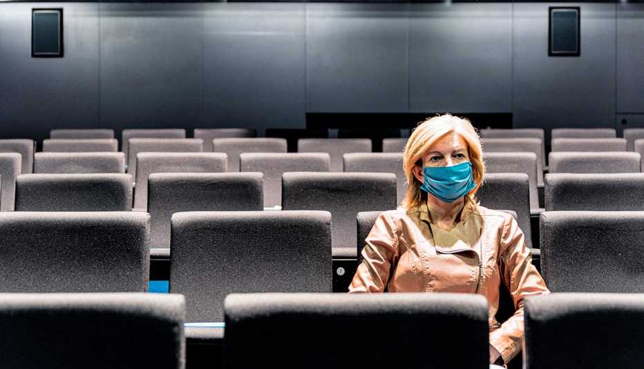 Una mujer que lleva una mascarilla protectora sentada en un cine vacío.