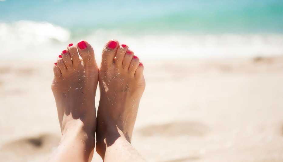 Los pies de una mujer en una playa reflejan la salud y los cuidados a tener en un salón de uñas