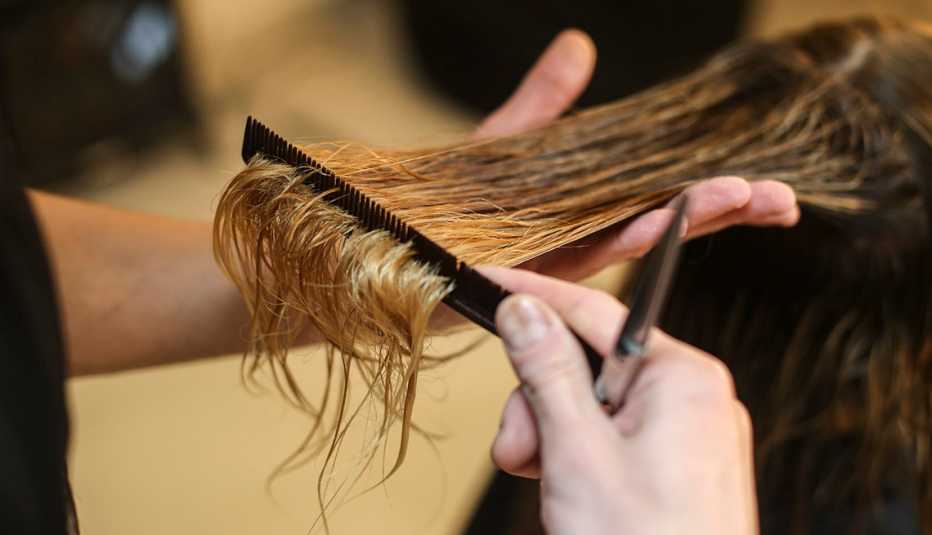 Un primer plano de una persona cortando el cabello de una mujer en una peluquería.