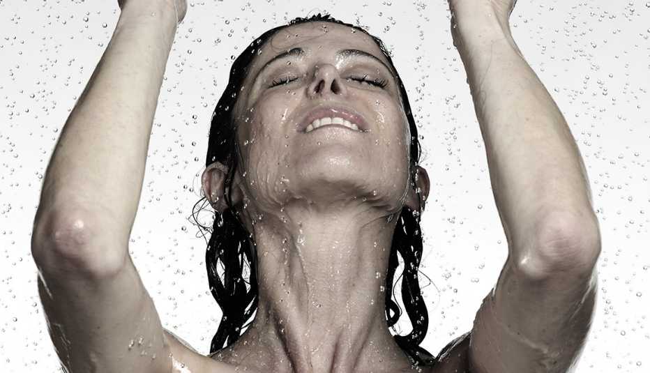 Mujer con los ojos cerrados y los brazos levantados mientras le cae agua.