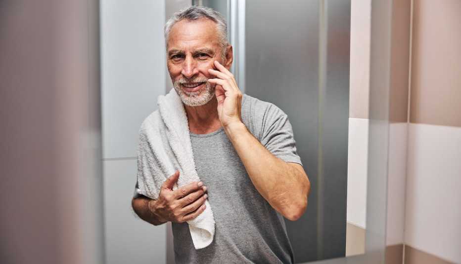 Un hombre se toca su rostro mientras se mira en el espejo del baño.
