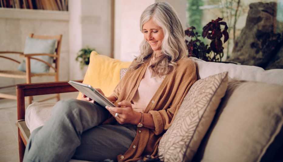 Mujer sentada en un sofá y mirando una tableta.