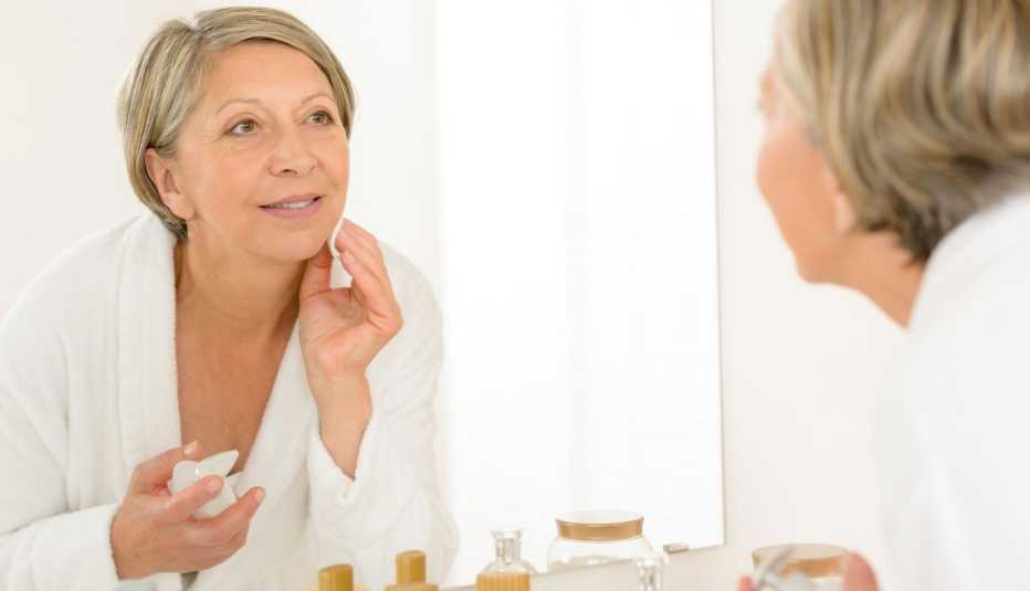 Mujer mayor limpiándose la cara frente a un espejo.
