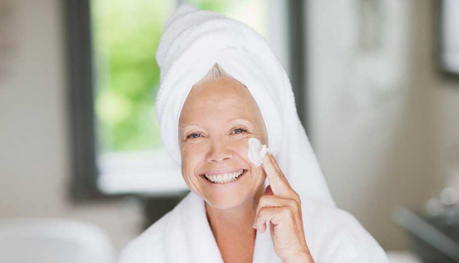 Mujer en bata de baño y aplicándose una crema en la cara