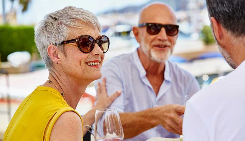 Dos hombres y una mujer con lentes de sol sentados en una mesa en el patio de un restaurante.
