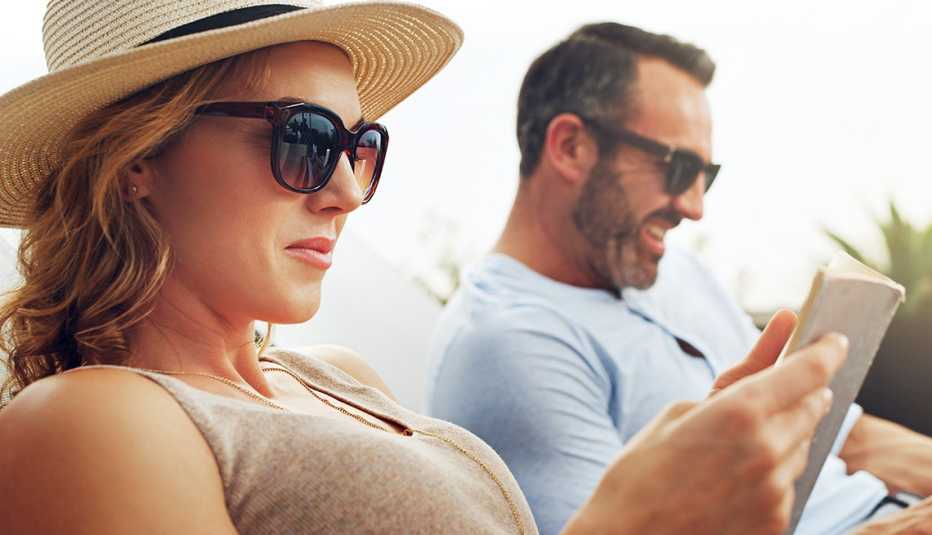 Pareja sentada en sillas de playa con lentes de sol y mirando sus teléfonos móviles.