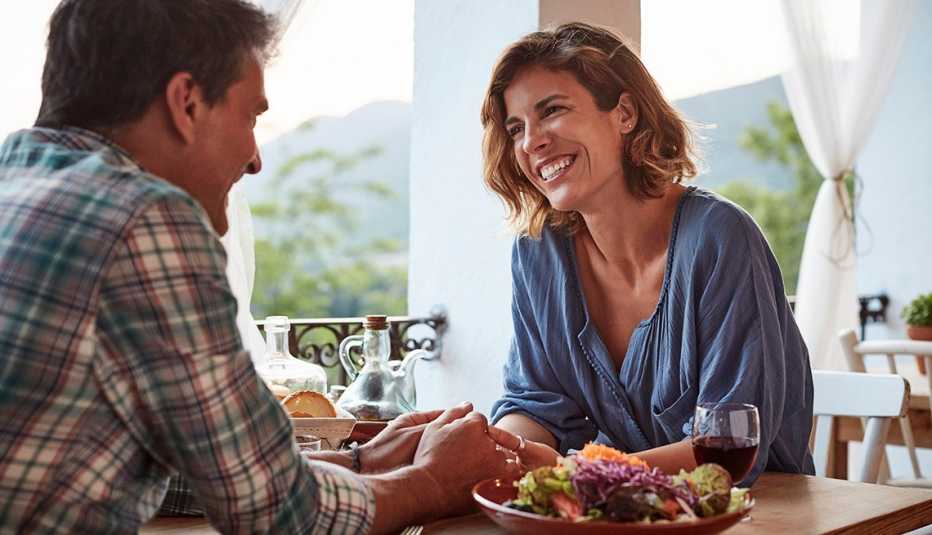 Una pareja de hombre y mujer luciendo feliz mientras se toman de la mano sentados en un restaurante.