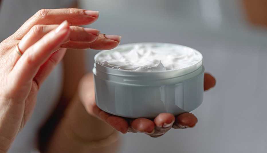 Primer plano de mujer con crema hidratante para una piel limpia y suave, sosteniendo el tarro de crema en las manos.