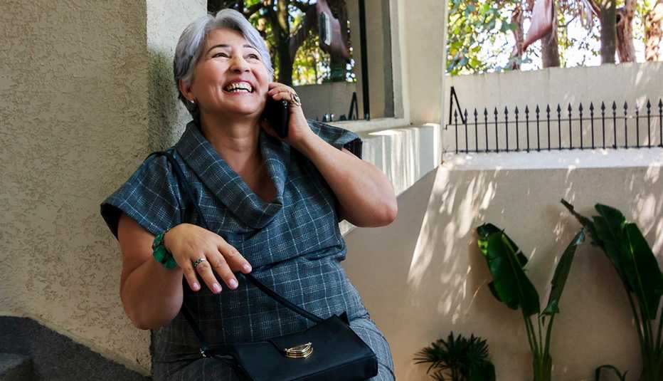 Una mujer está sonriendo mientras habla por un teléfono celular afuera.