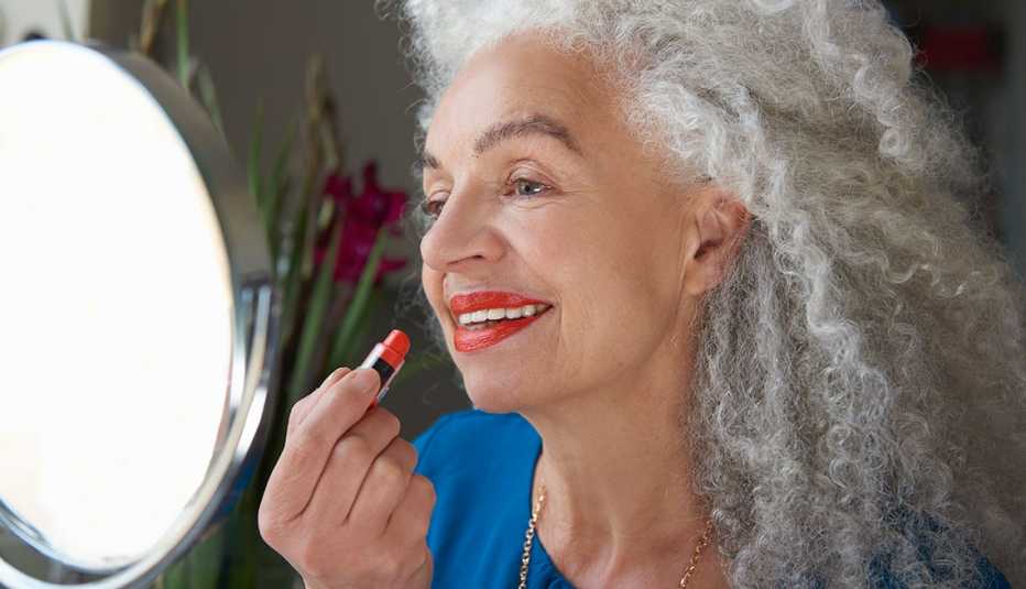 Una mujer aplicando un lápiz labial color rojo mientras se mira al espejo.