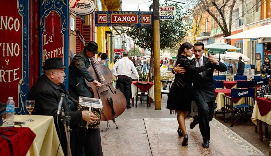 Una pareja bailando tango en una acera de Buenos Aires mientrasd dos músicos tocan sus instrumentos