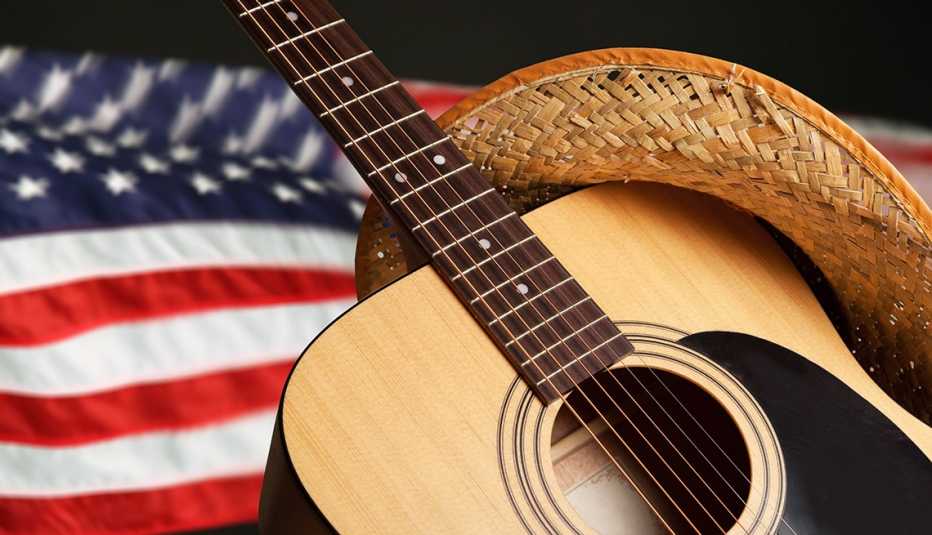 Una guitarra acústica con sombrero de vaquero frente a una bandera estadounidense.