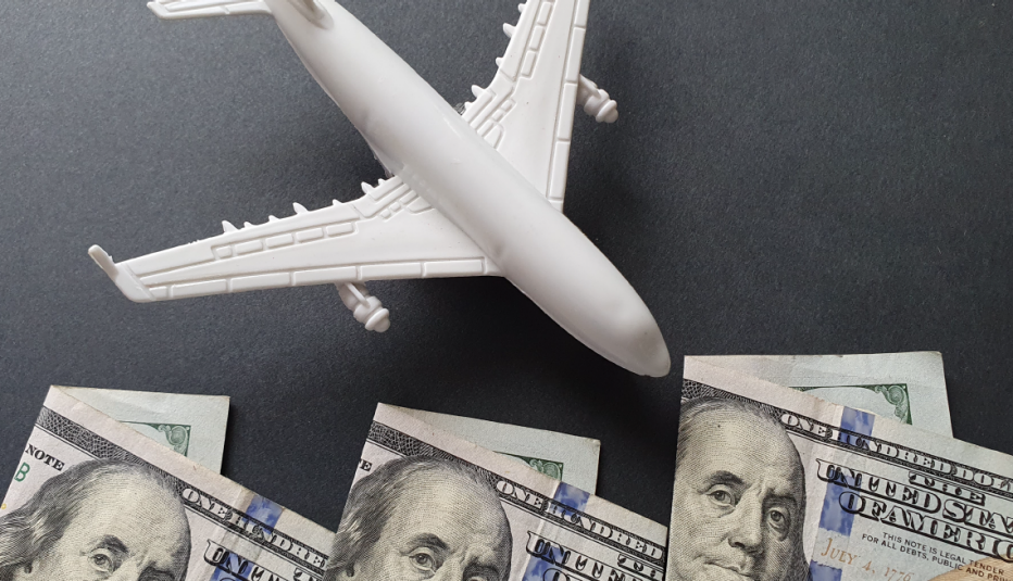 Tres billetes de cien dólares y un avión blanco sobre fondo gris