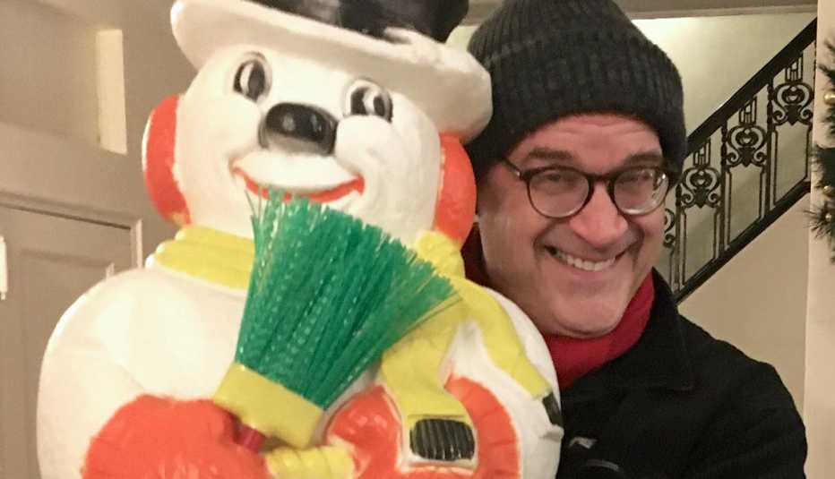 Hombre sujeta un muñeco de nieve mientras sonríe