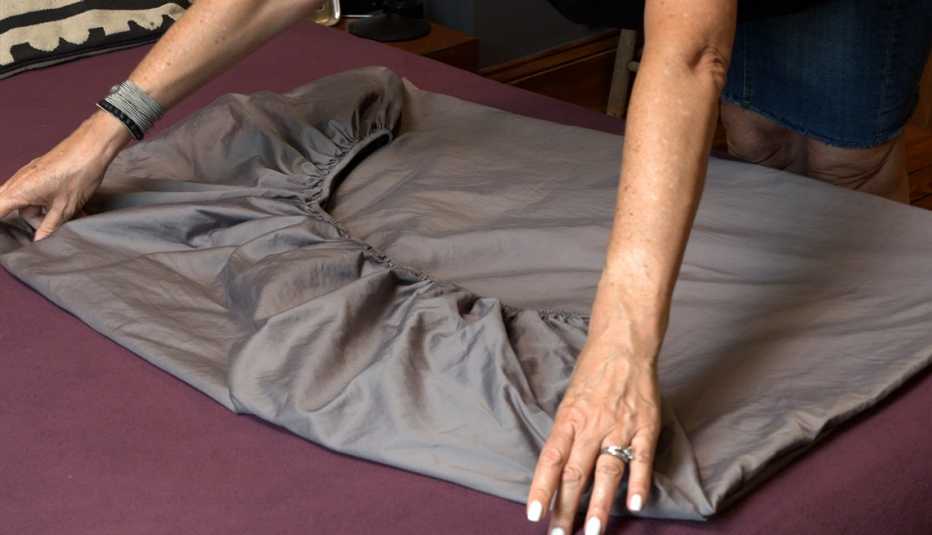 Persona alisa los bordes de una sábana ajustable parcialmente plegada