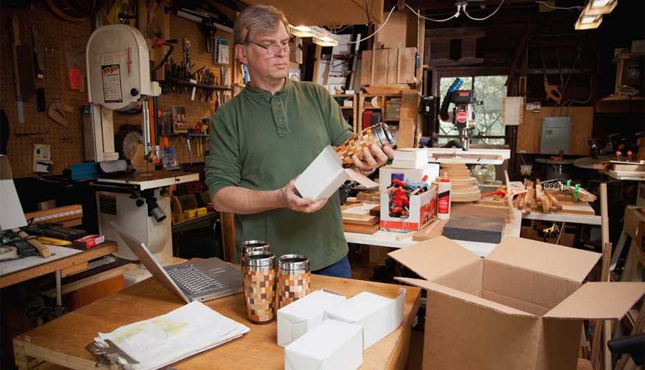 Hombre empaca tazas de madera artesanales en cajas de cartón