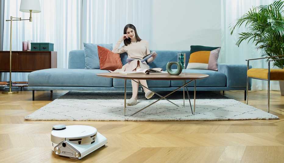Mujer sentada en el sofá mira trabajar a la aspiradora Samsung JetBot 90