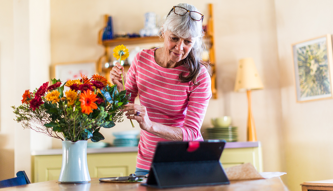 Mujer hace un arreglo de flores mientras ve un tutorial en una tableta