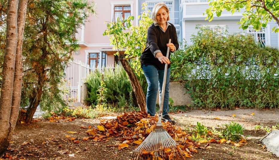 Mujer rastrilla hojas de otoño en su jardín