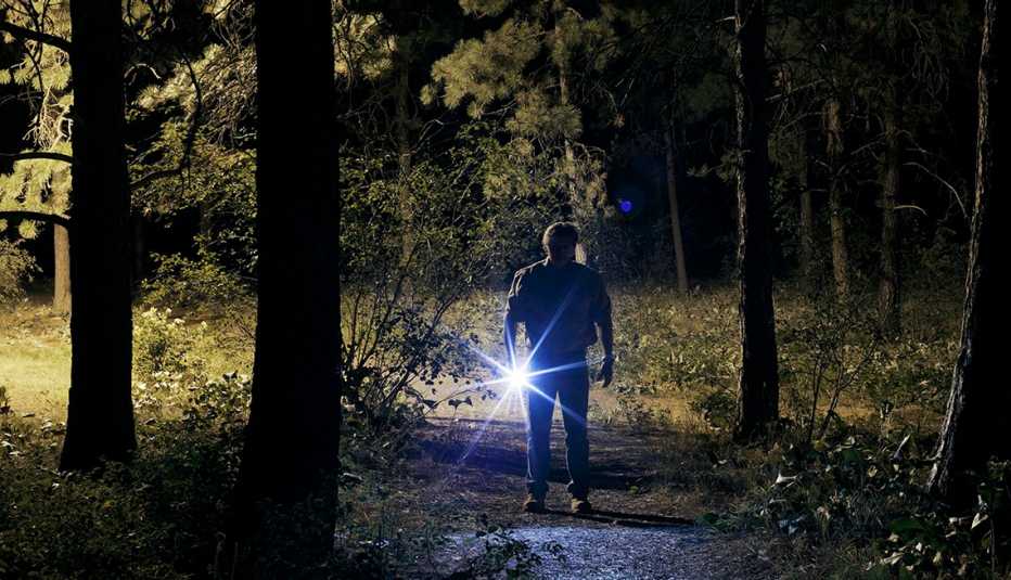 Un hombre sujeta una linterna en un bosque de noche.