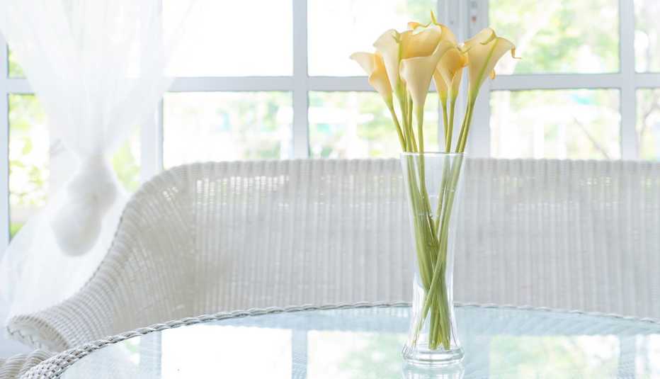 Flores amarillas en un vaso en una mesa de vidrio con una silla decorativa detrás