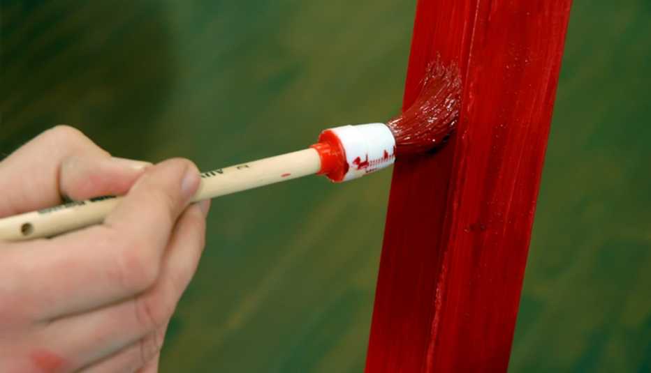 Acercamiento de una persona pintando un mueble con pintura roja