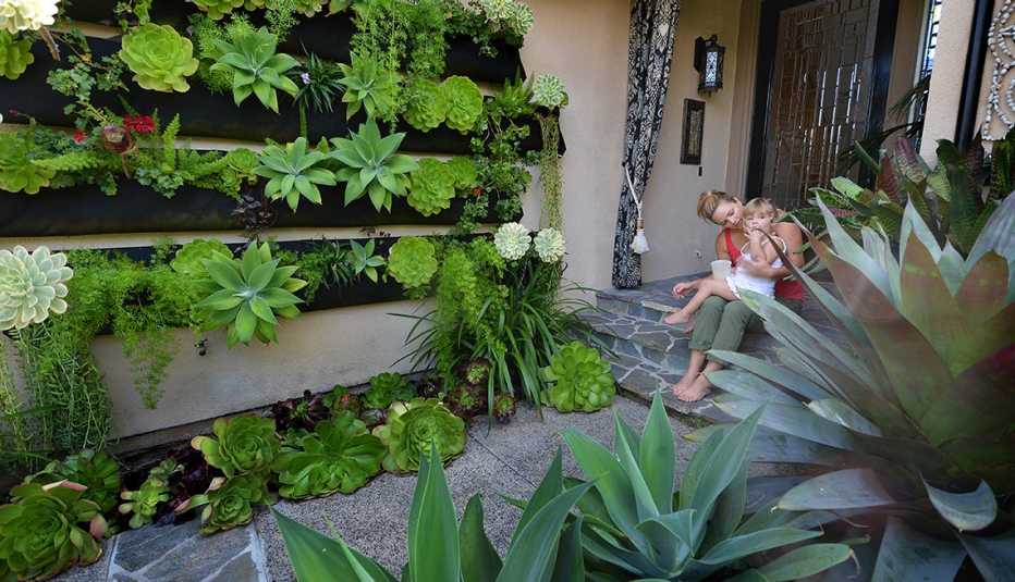 Mujer con una niña pequeña afuera de su casa en frente de un jardín vertical