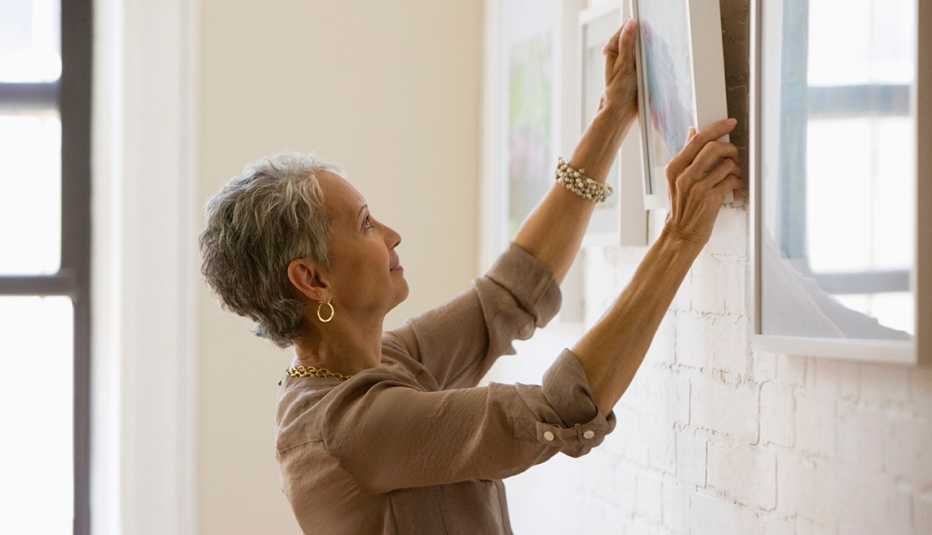 Mujer colgando cuadros en una pared de ladrillos blancos