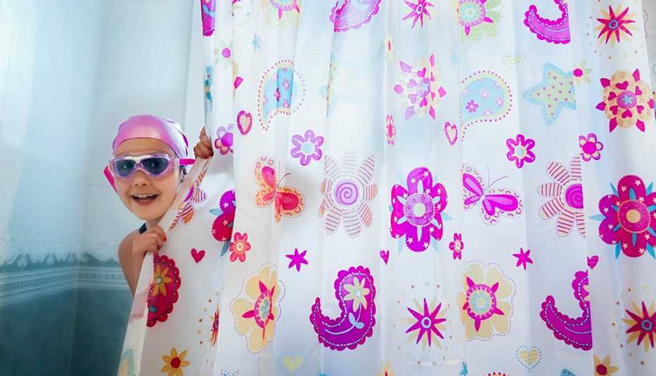 Niño con gorro y gafas de natación asomándose detrás de una cortina baño colorida.