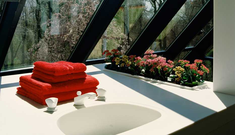 Un baño lleno de luz con dos toallas rojas sobre el lavamanos