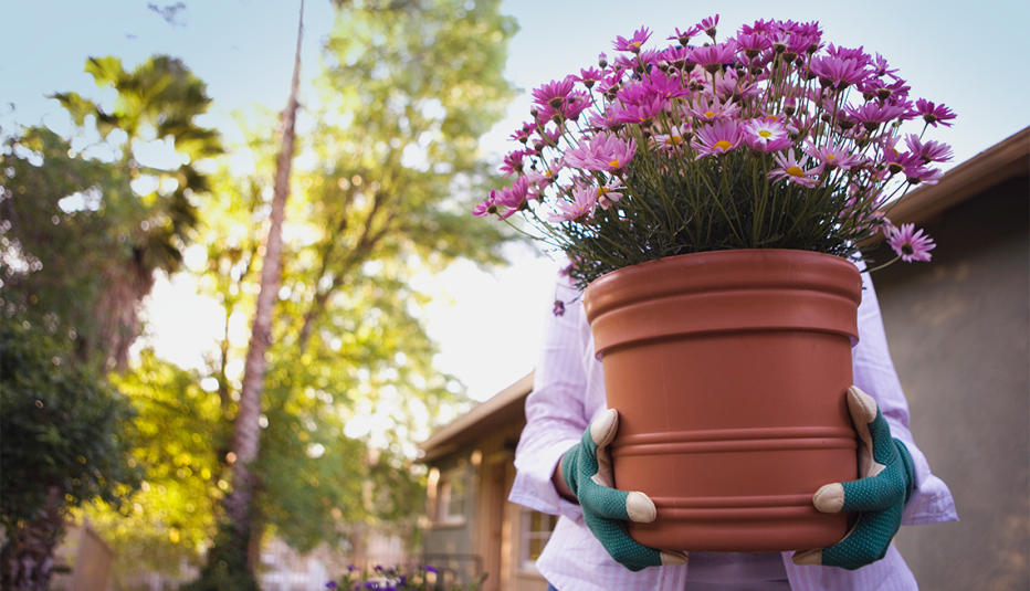 Una jardinera llevando una olla de barro con flores