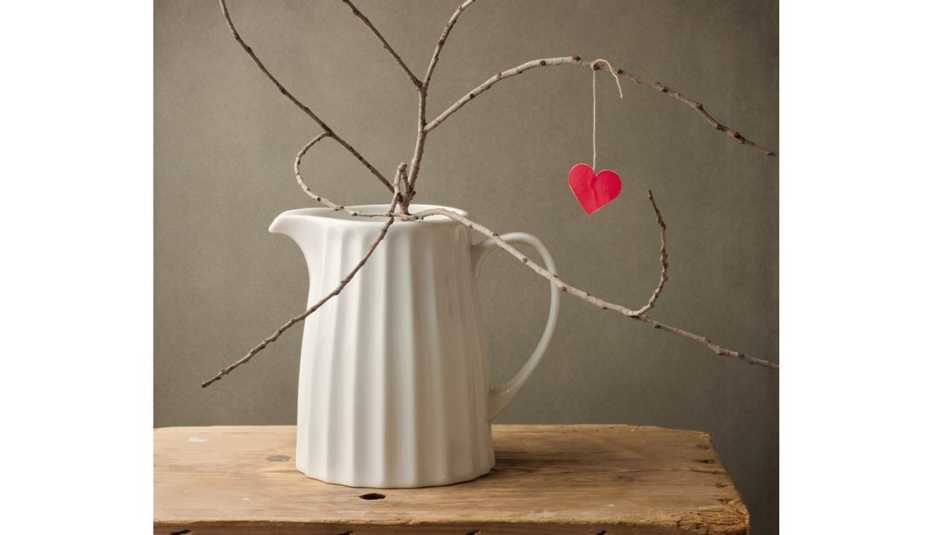 Jarra blanca de porcelana con una rama y un corazón de papel