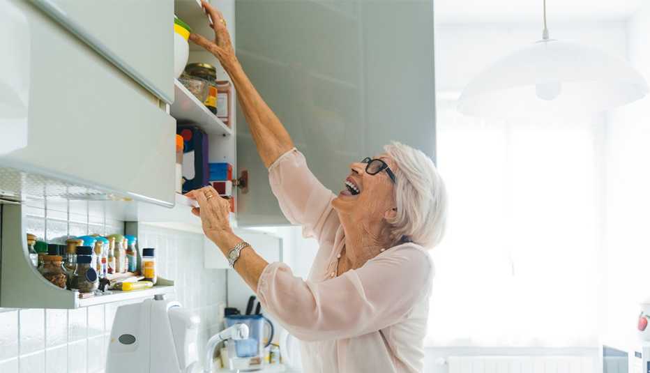 Mujer alcanza un artículo en un gabinete alto de la cocina