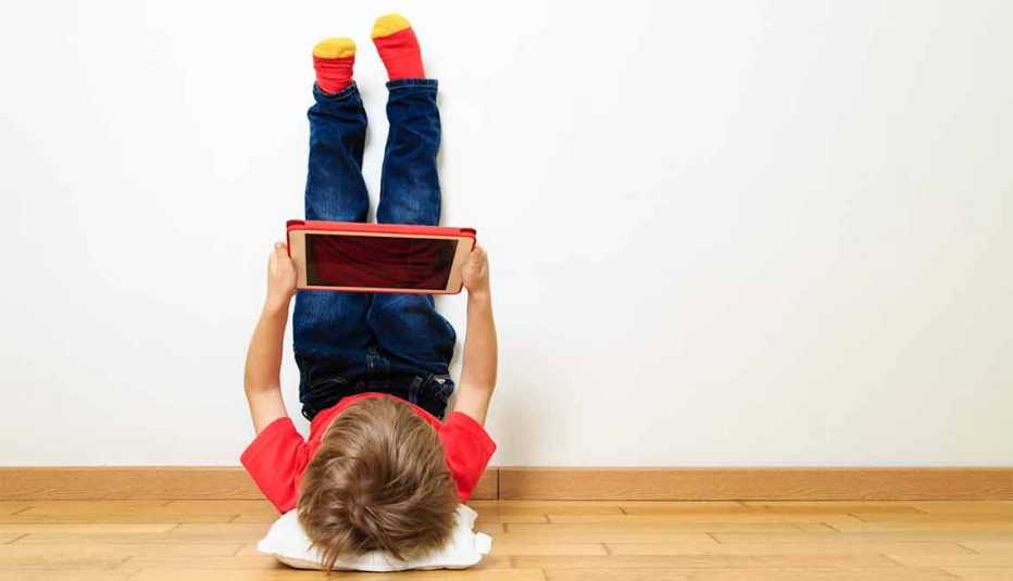 Niño con los pies apoyados en la pared sosteniendo una tableta en sus manos