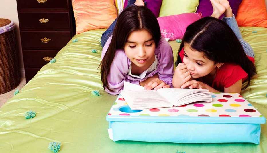 Dos niñas leyendo un libro sobre un cojín para computadoras