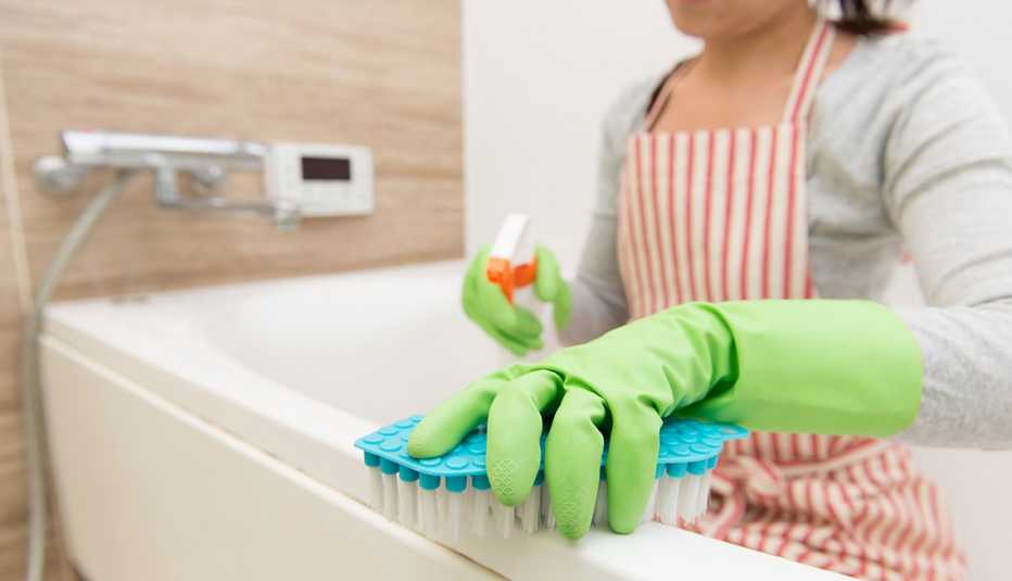 Cómo deshacerte del moho - Mujer limpiando la bañera