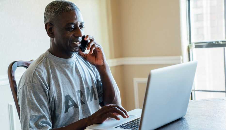 Hombre usando el computador mientras habla por teléfono.