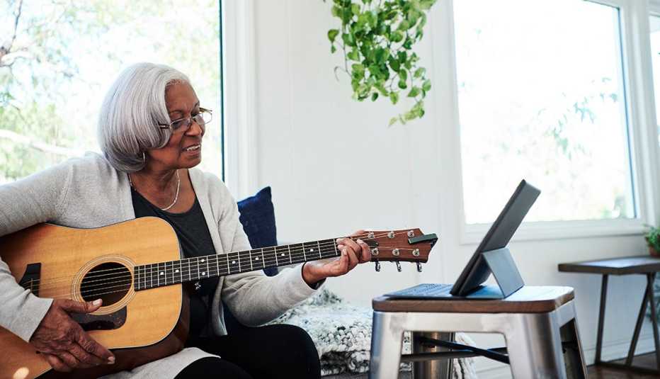 Mujer aprendiendo a tocar guitarra observa su tableta digital
