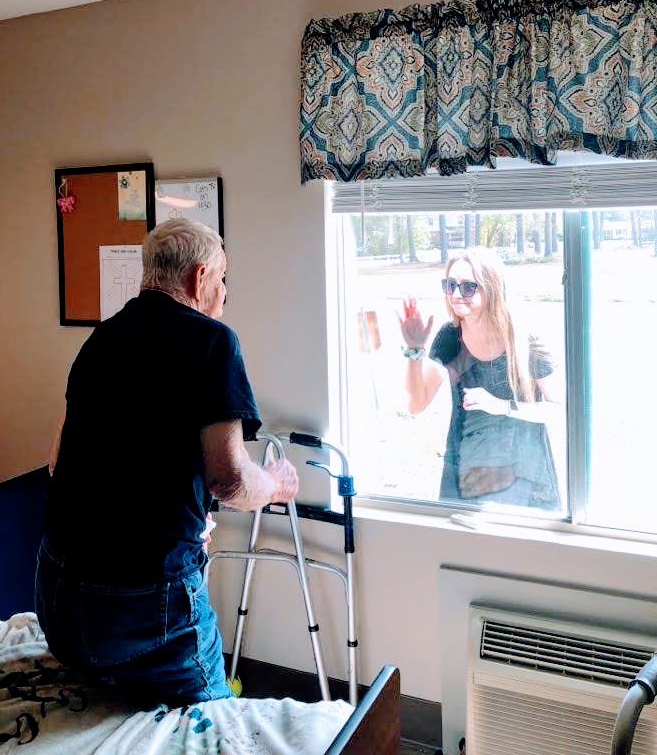 Un hombre mayor recibe una visita de su hija a través de la ventana de su unidad de la planta baja