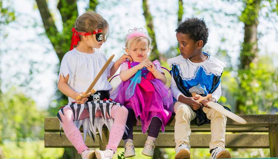 Tres niños sentados en un banco del parque vistiendo disfraces caseros de halloween