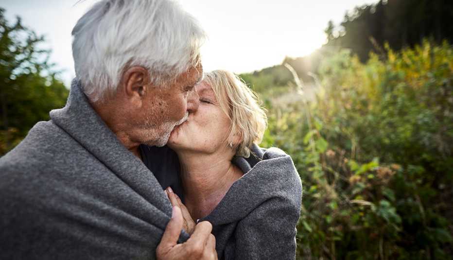 Una pareja de adultos mayores se arropan con una manta y se dan un beso