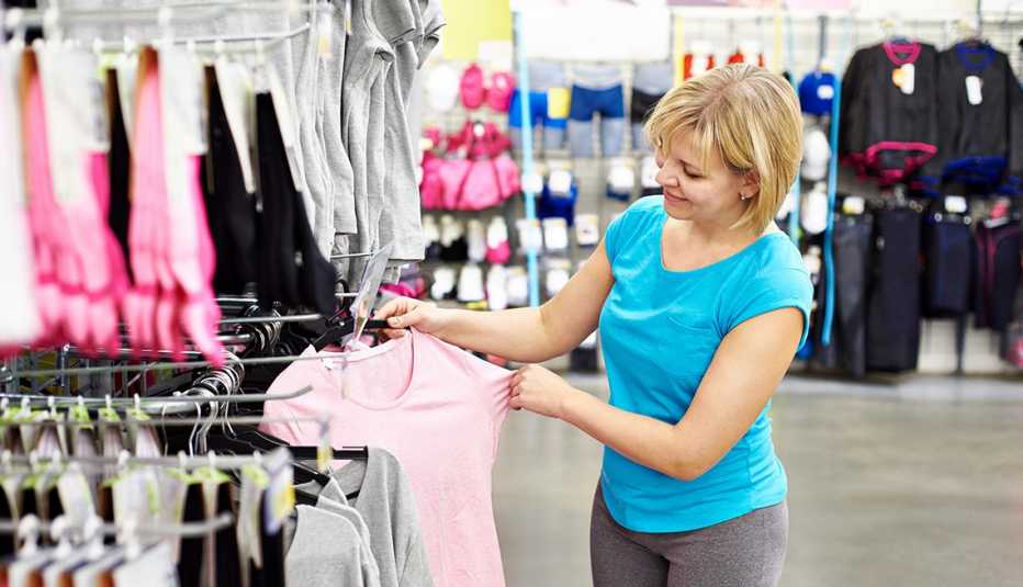 Una mujer mirando una camiseta rosa en una tienda de ropa deportiva.