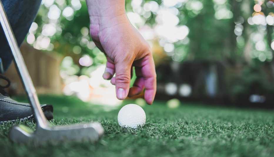 Imagen de una mano alcanzando una pelota de golf en el suelo con un palo de golf