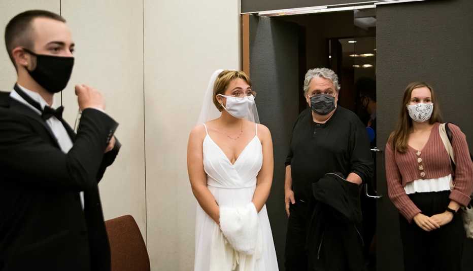 Pareja joven con máscaras se preparan para entrar a la ceremonia de su boda