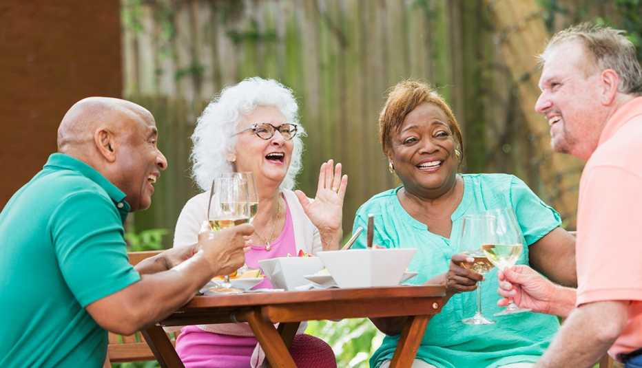 Cuatro personas están sentadas alrededor de una mesa pequeña, hablando, riendo y bebiendo vino blanco